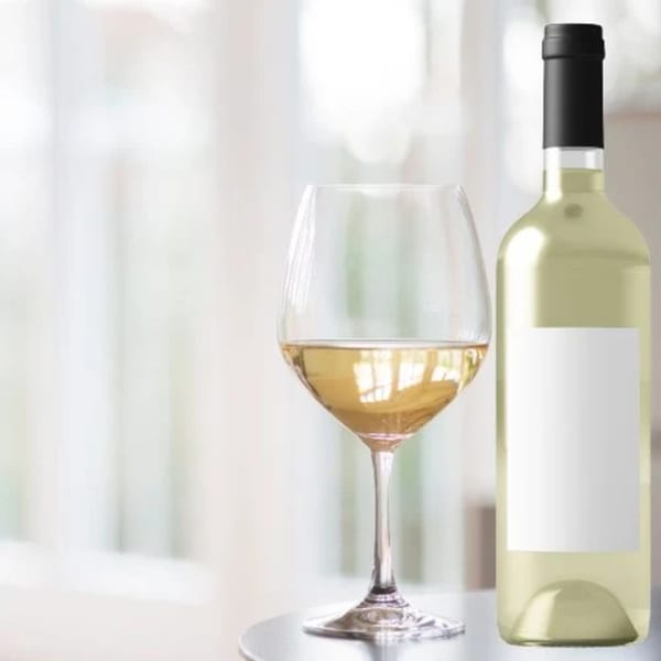 A glass of white wine next to a bottle of white wine on a table.