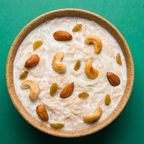 A bowl of Indian vermicelli kheer with cashews, almonds, and raisins on a green background.