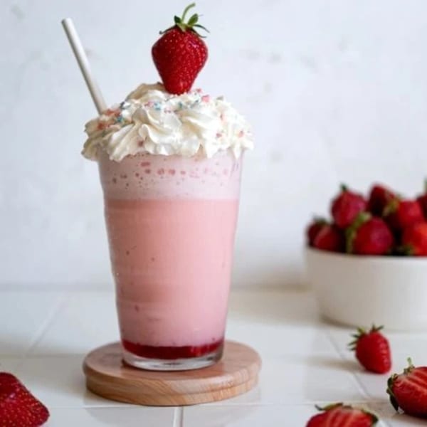 Pink strawberry milkshake with whipped cream, sprinkles, and a fresh strawberry on top.