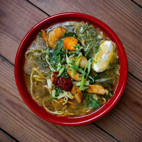 A vibrant red bowl of Everest Nepalese & Indian Cuisine's noodle soup with chicken, shrimp, and lemon.