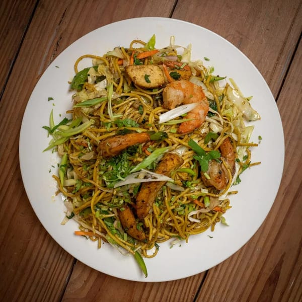 A white plate of Everest Nepalese & Indian Cuisine's noodles with shrimp, chicken, and vegetables.