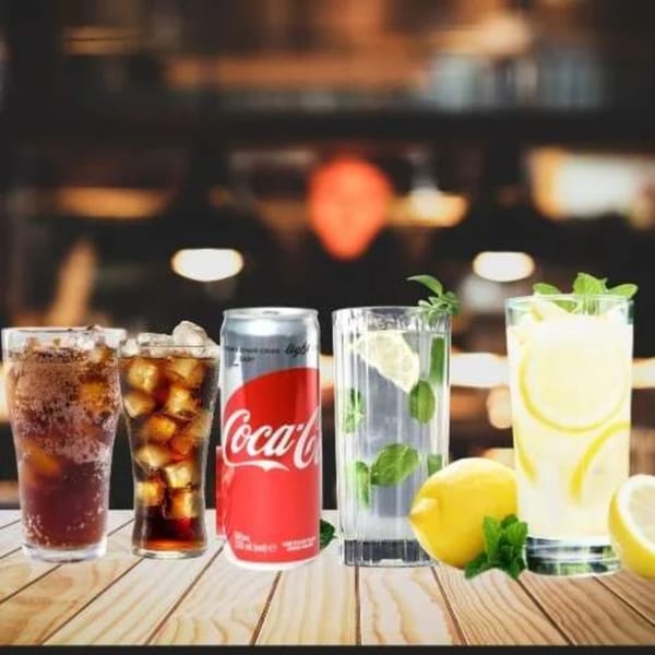 Assortment of cold beverages including Coca-Cola, sparkling water with mint, and lemonade on a wooden table.