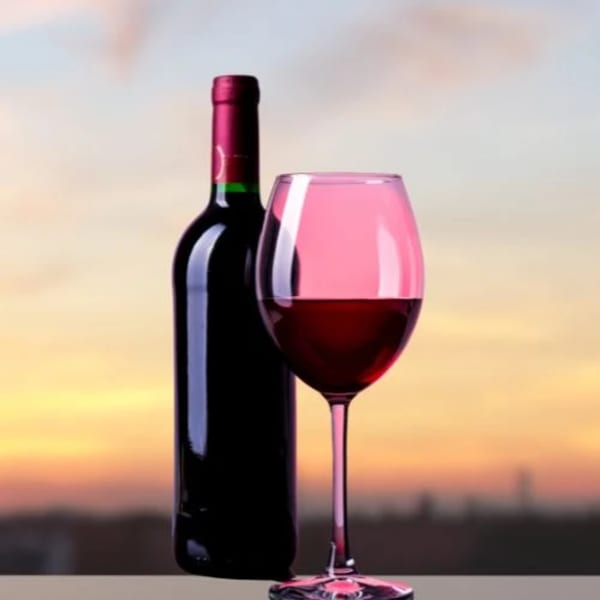 A bottle of red wine and a glass of red wine with a sunset in the background.