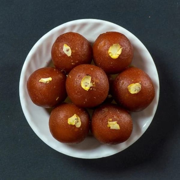 Seven Gulab Jamun, Indian fried dough balls, garnished with nuts on a white plate.