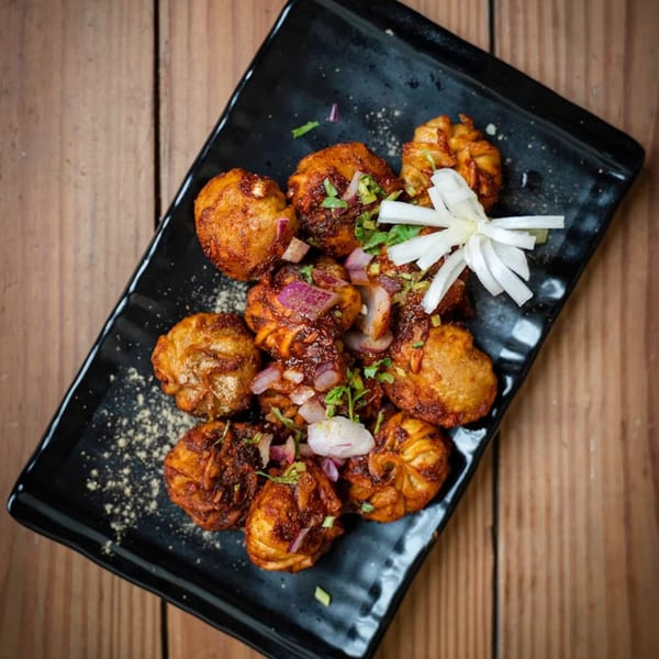 Spicy fried momos garnished with red onions, cilantro, and white radish on a black plate.