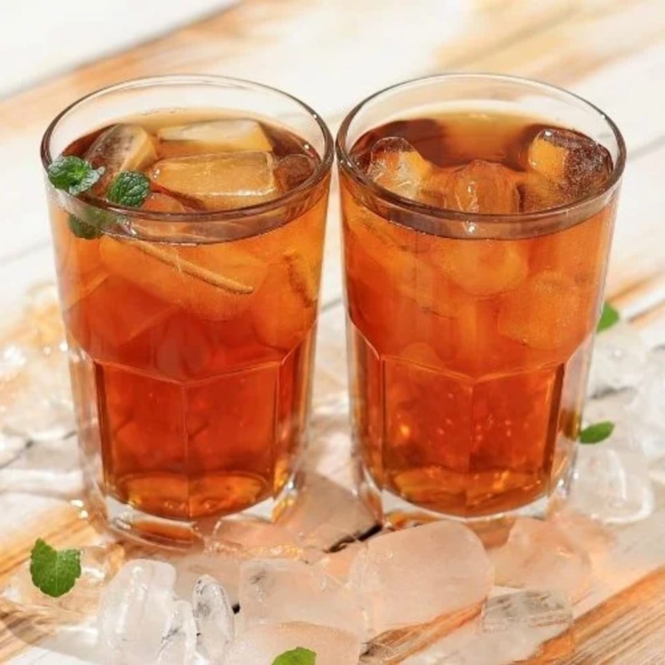 Two glasses of iced tea with mint leaves and ice cubes on a wooden surface.