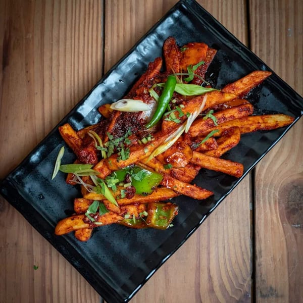 Chili potato fries, garnished with green chilies, bell peppers, and herbs on a black plate.