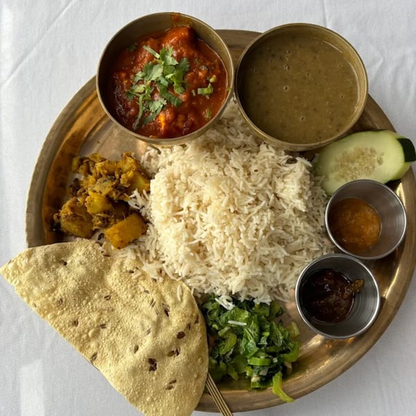 A traditional Indian thali with rice, curries, vegetables, papadum, and chutneys on a brass plate.