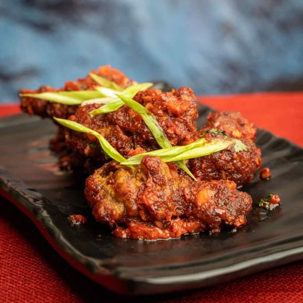 Spicy Indian chicken wings, garnished with green onions, served on a black rectangular plate.