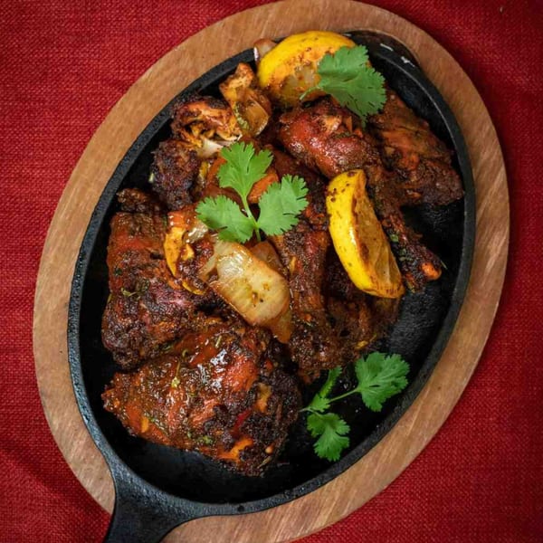Sizzling Indian chicken tikka with onions, lemon wedges, and cilantro on a cast iron platter.
